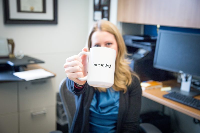 Heather Hayenga holding a mug that reads "I'm funded"